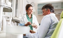 Smiling dentist showing patient model of teeth