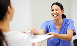 Smiling dental assistant handing patient form