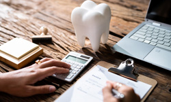 Filling out form on clipboard on desk with laptop and tooth shaped paperweight