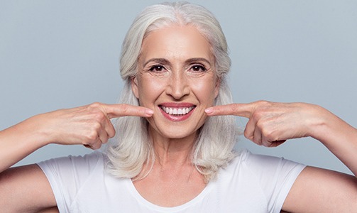Older woman pointing at her beautiful smile with zirconia dental implants