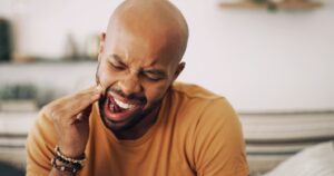 Man holding jaw and wincing in pain from tooth sensitivity.